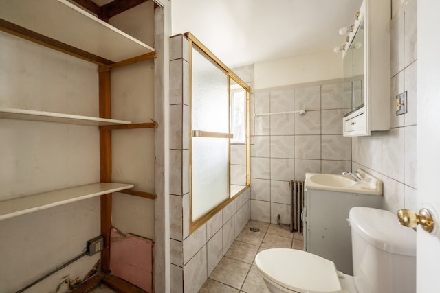 bathroom with a shower with door, tile patterned flooring, radiator, vanity, and tile walls