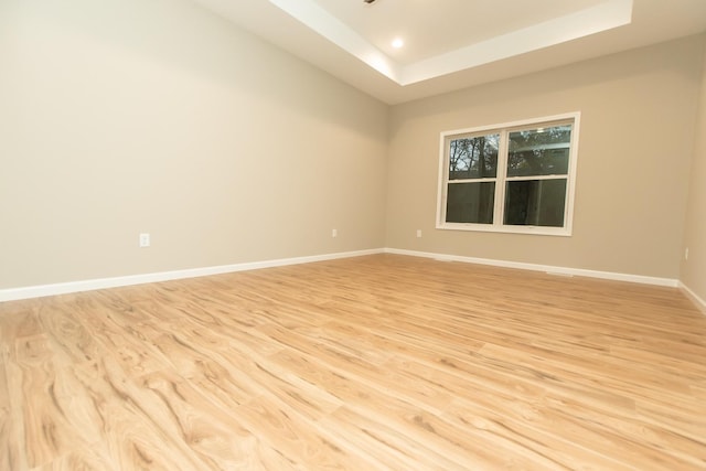 spare room with light wood-type flooring, baseboards, a tray ceiling, and recessed lighting
