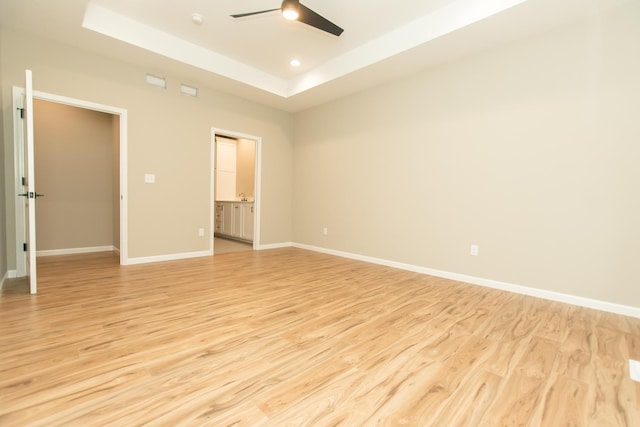 spare room featuring ceiling fan, light wood-type flooring, baseboards, and a tray ceiling
