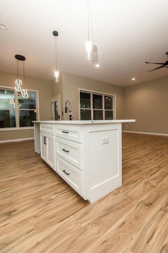 kitchen featuring an island with sink, white cabinets, light wood finished floors, and pendant lighting