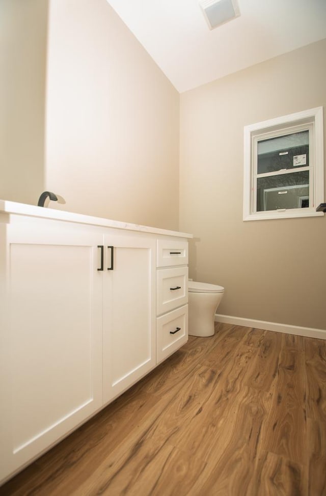 bathroom with wood finished floors, toilet, vaulted ceiling, and baseboards