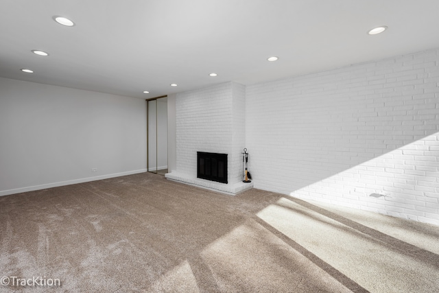 unfurnished living room with a brick fireplace, brick wall, and carpet