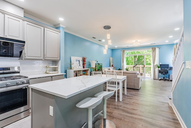 kitchen featuring a kitchen bar, light hardwood / wood-style floors, decorative backsplash, gas range, and pendant lighting