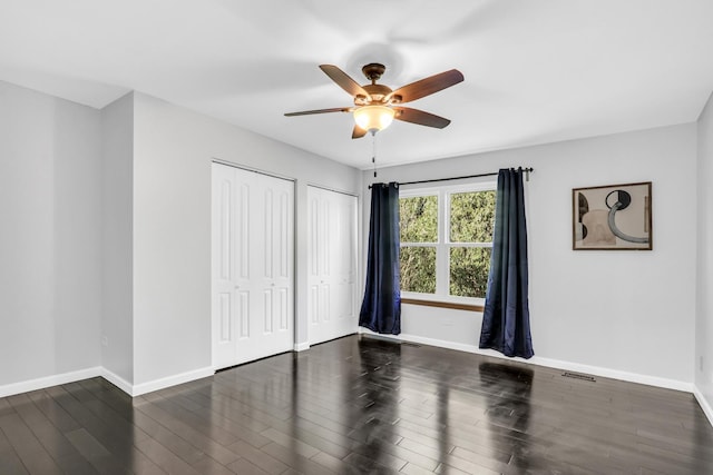 unfurnished bedroom with multiple closets, ceiling fan, and dark hardwood / wood-style flooring