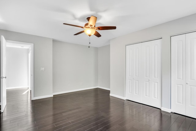 unfurnished bedroom with ceiling fan, dark wood-type flooring, and two closets