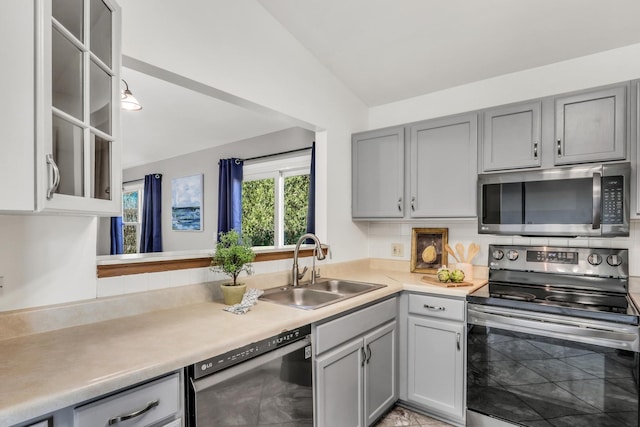 kitchen featuring decorative backsplash, gray cabinetry, stainless steel appliances, sink, and lofted ceiling