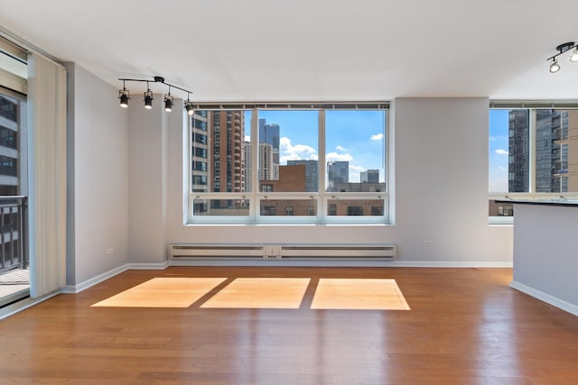 empty room with a baseboard heating unit, hardwood / wood-style floors, and plenty of natural light