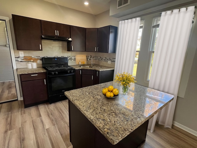 kitchen featuring dark brown cabinetry, light hardwood / wood-style floors, sink, black gas range, and a center island