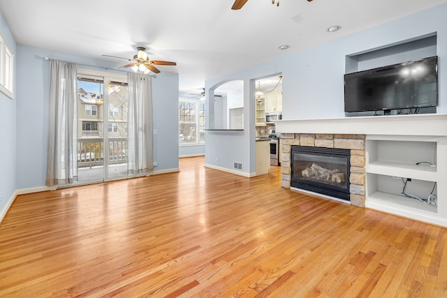 unfurnished living room with ceiling fan, a stone fireplace, and light hardwood / wood-style flooring