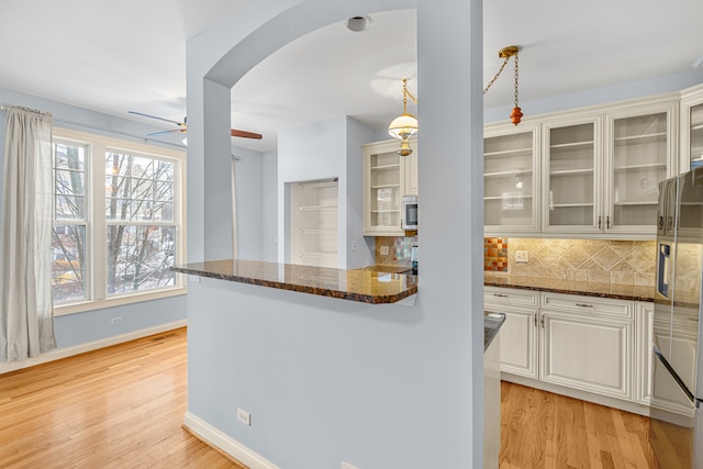 kitchen with decorative backsplash, hanging light fixtures, dark stone counters, and light wood-type flooring