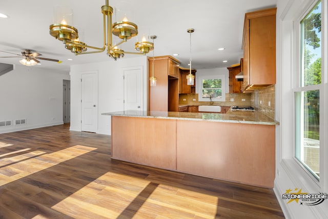 kitchen with kitchen peninsula, hardwood / wood-style floors, backsplash, and light stone countertops