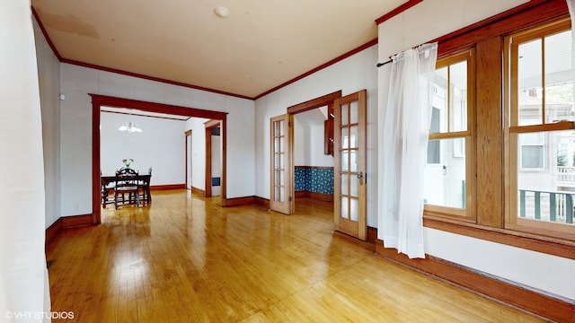 empty room featuring light wood-type flooring, a chandelier, french doors, and ornamental molding