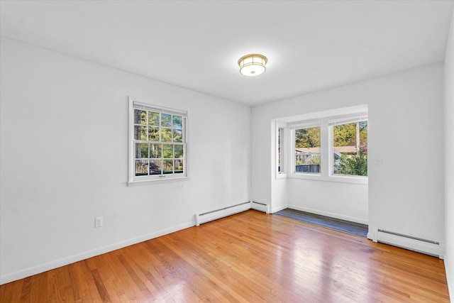 spare room with a wealth of natural light, baseboard heating, and wood-type flooring