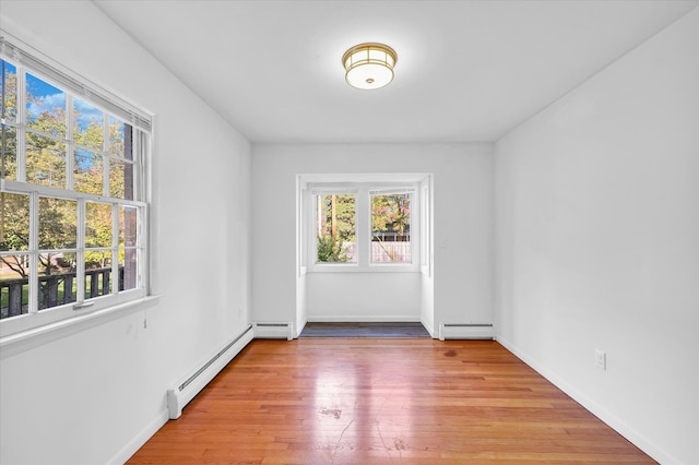 empty room with light hardwood / wood-style floors, baseboard heating, and a healthy amount of sunlight