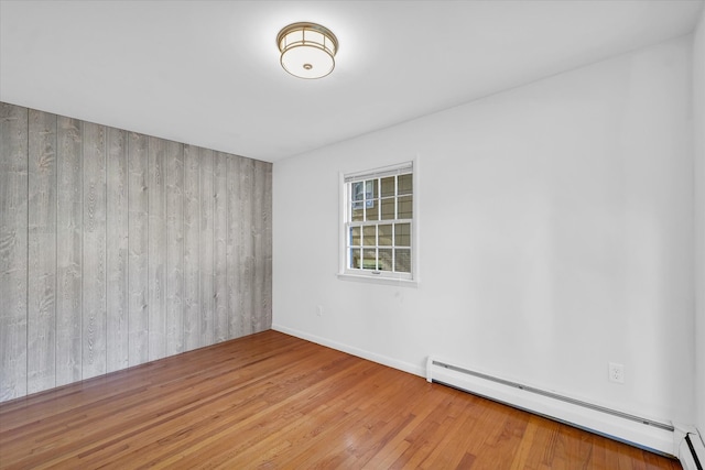 unfurnished room featuring a baseboard heating unit, wood walls, and wood-type flooring