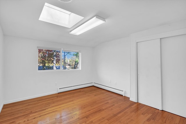 unfurnished bedroom featuring light wood-type flooring, a skylight, and baseboard heating