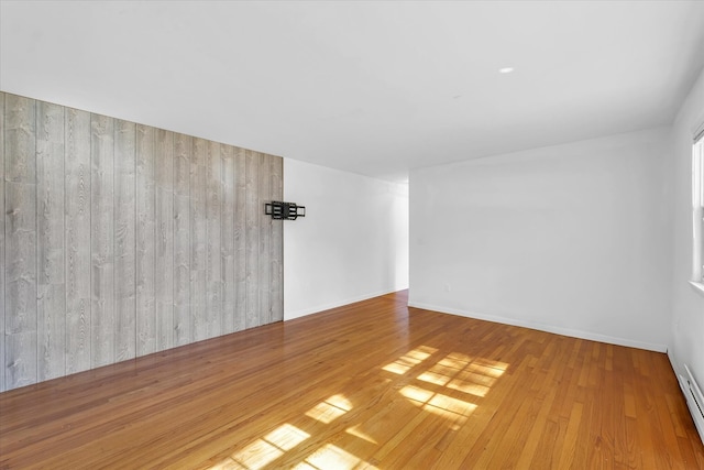 unfurnished room featuring wood walls, baseboard heating, and light hardwood / wood-style flooring