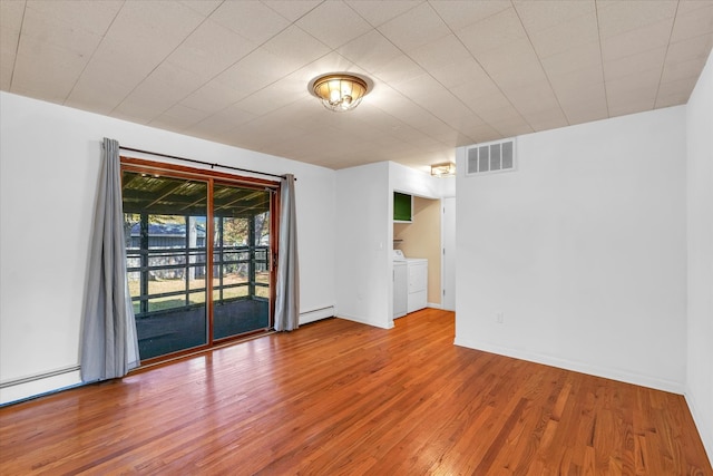 empty room featuring washing machine and dryer, hardwood / wood-style flooring, and a baseboard radiator