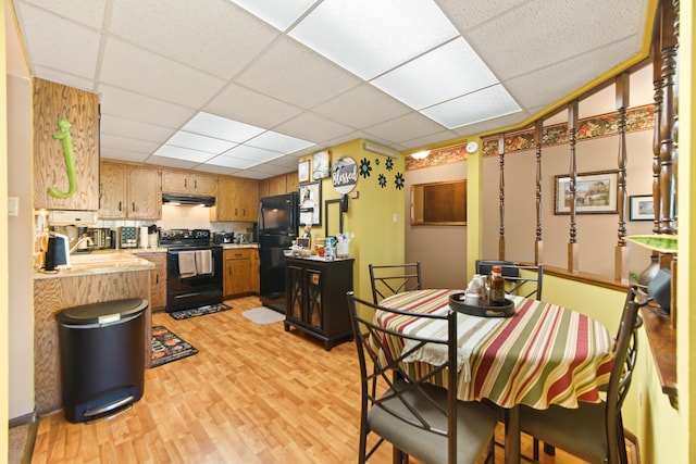 kitchen featuring a drop ceiling, light wood-type flooring, black appliances, and sink