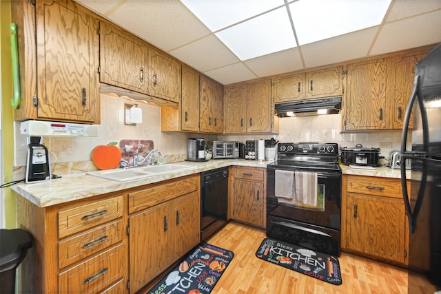 kitchen with a paneled ceiling, sink, black appliances, tasteful backsplash, and light wood-type flooring