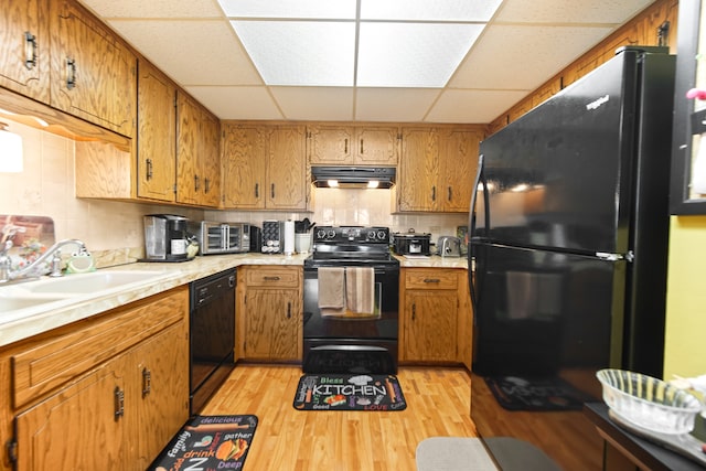 kitchen featuring light hardwood / wood-style flooring, black appliances, sink, and a paneled ceiling