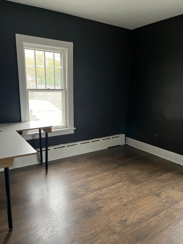 empty room featuring baseboard heating and dark hardwood / wood-style floors