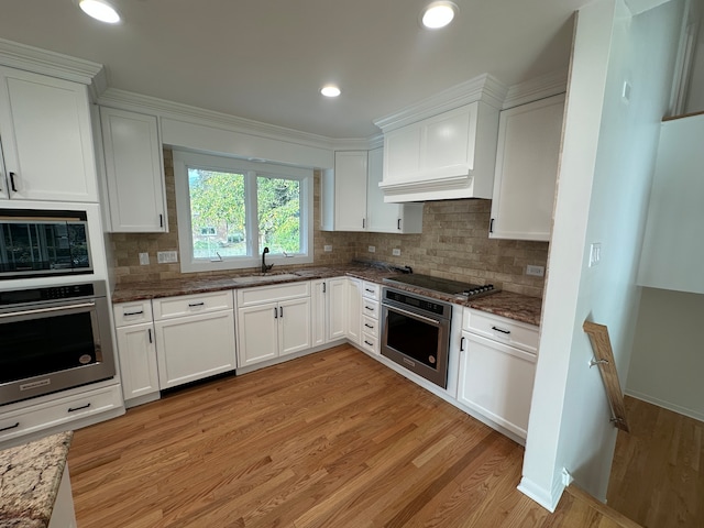 kitchen with tasteful backsplash, appliances with stainless steel finishes, light hardwood / wood-style floors, white cabinets, and dark stone countertops