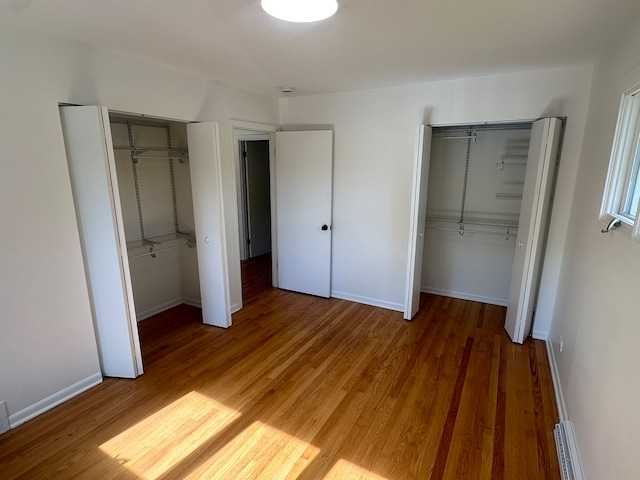 unfurnished bedroom with multiple closets, a baseboard radiator, and hardwood / wood-style flooring