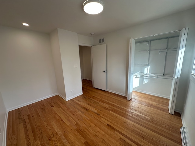 unfurnished bedroom featuring a closet, baseboard heating, and light hardwood / wood-style floors