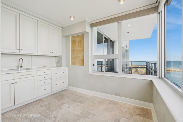 kitchen featuring a water view, white cabinetry, ornamental molding, and sink