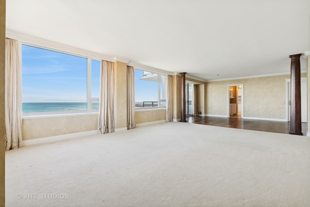 spare room with carpet, a water view, a beach view, ornamental molding, and decorative columns