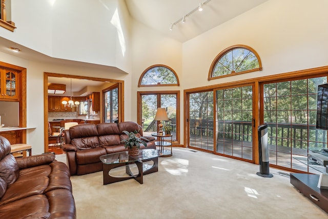 carpeted living room featuring rail lighting, a high ceiling, and an inviting chandelier