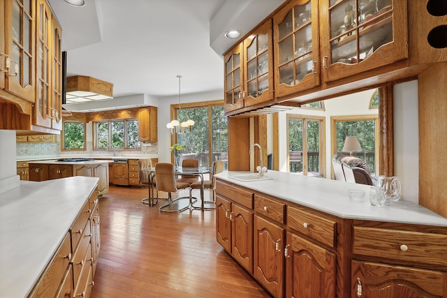 kitchen with a notable chandelier, pendant lighting, decorative backsplash, sink, and light hardwood / wood-style floors