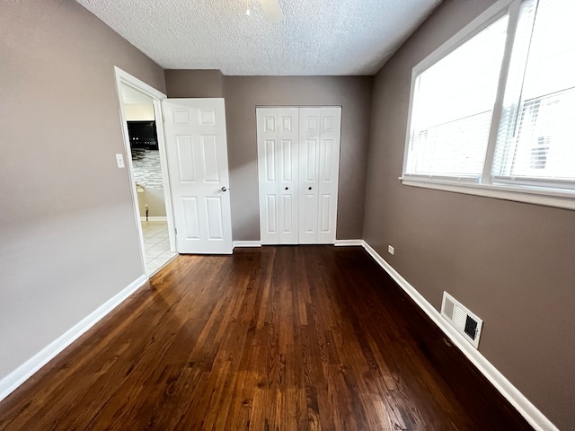 unfurnished bedroom featuring a textured ceiling, a closet, and dark hardwood / wood-style flooring