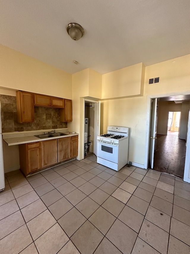 kitchen with white range with gas stovetop, light tile patterned floors, and sink