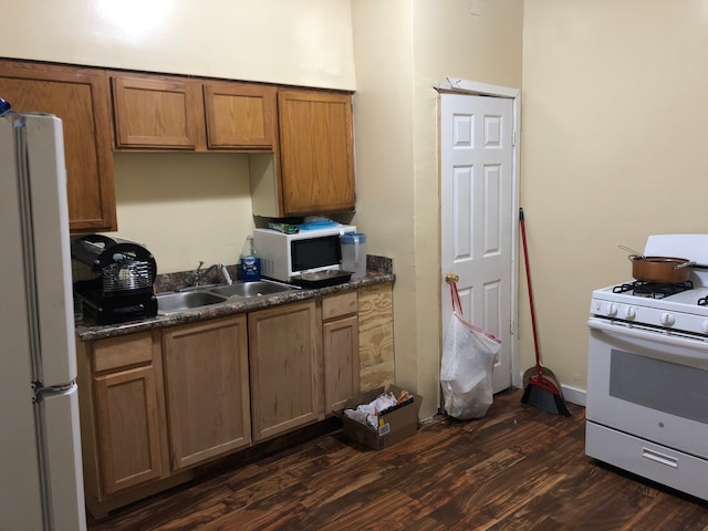 kitchen featuring white appliances, dark hardwood / wood-style floors, dark stone countertops, and sink