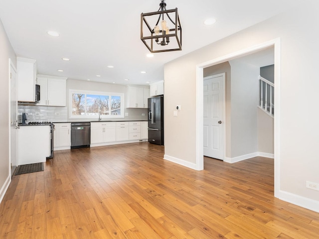 kitchen featuring white cabinetry, hanging light fixtures, light hardwood / wood-style flooring, backsplash, and stainless steel appliances