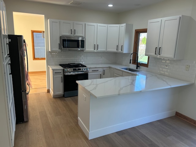 kitchen with stainless steel appliances, light stone countertops, light hardwood / wood-style floors, white cabinets, and kitchen peninsula