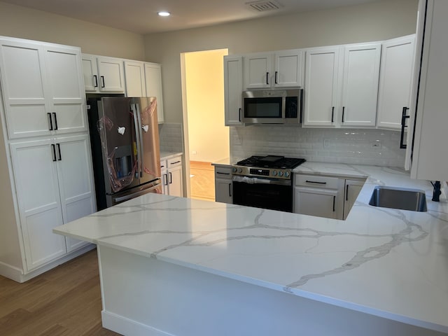 kitchen with stainless steel appliances, white cabinetry, kitchen peninsula, and light stone counters