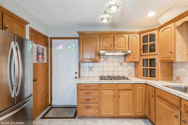 kitchen featuring under cabinet range hood, stainless steel appliances, glass insert cabinets, and tasteful backsplash