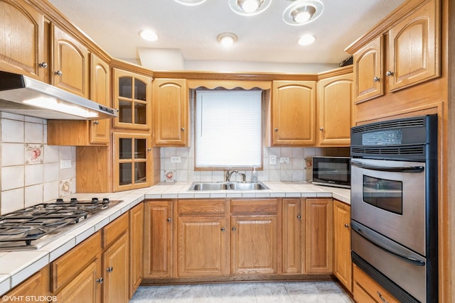 kitchen featuring under cabinet range hood, tile countertops, stainless steel appliances, a warming drawer, and a sink