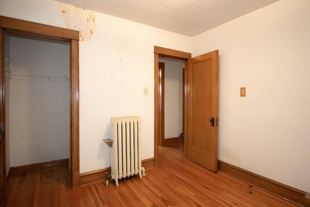 unfurnished bedroom with hardwood / wood-style flooring, radiator heating unit, and a closet