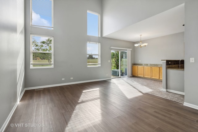 unfurnished living room with dark hardwood / wood-style flooring, a chandelier, and a towering ceiling