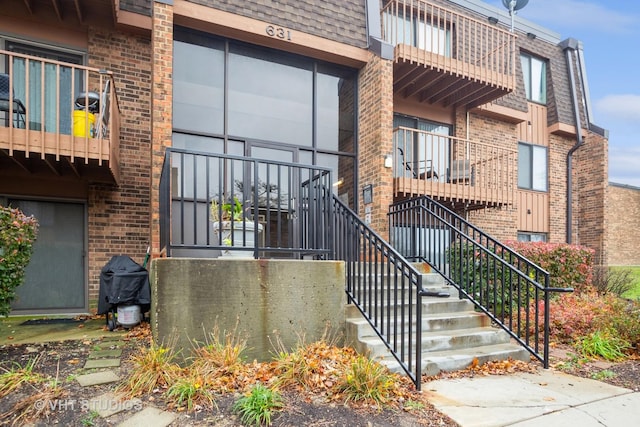 doorway to property with mansard roof, brick siding, and roof with shingles