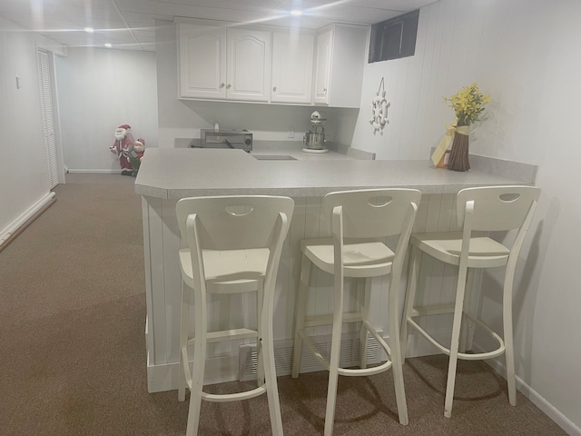 kitchen with carpet, a kitchen breakfast bar, white cabinetry, and kitchen peninsula