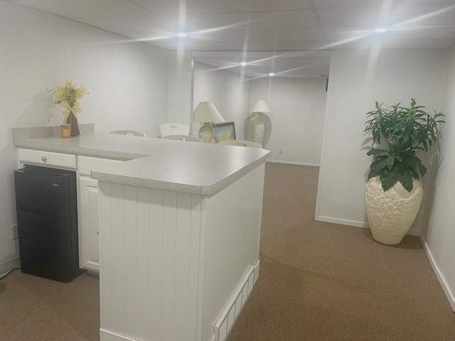 interior space featuring white cabinets, a paneled ceiling, and dark carpet