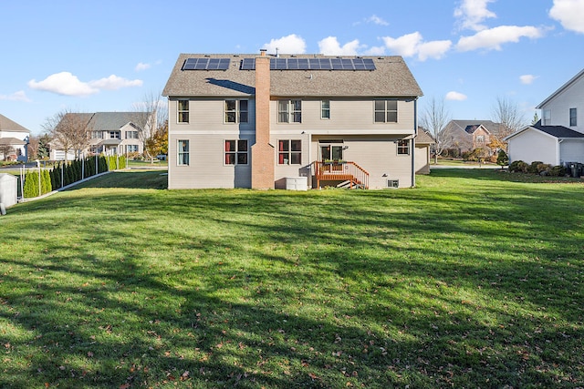 rear view of house with solar panels, a wooden deck, and a yard