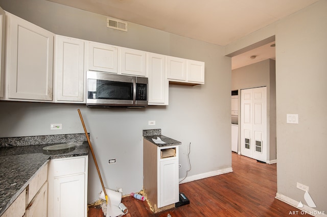 kitchen featuring dark wood-type flooring, dark stone countertops, and white cabinets