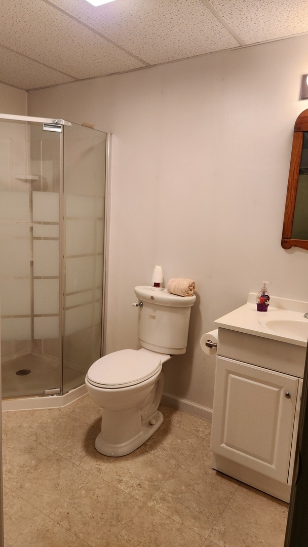 bathroom featuring a drop ceiling, toilet, a shower with door, and vanity