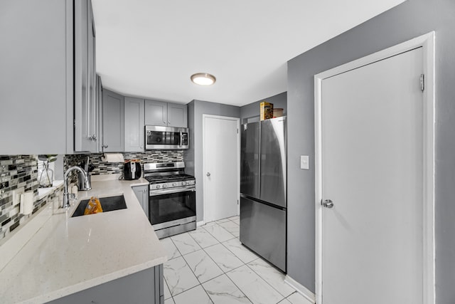 kitchen featuring light stone counters, backsplash, appliances with stainless steel finishes, gray cabinets, and sink